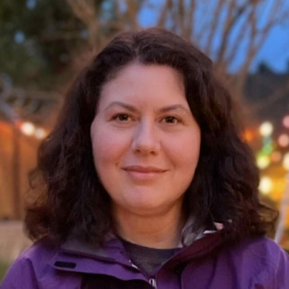 Headshot of Laura, wearing a purple coat with long brown hair.